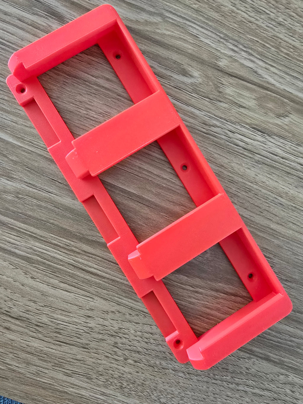 3D printed battery holder in red/coral colour on wooden surface