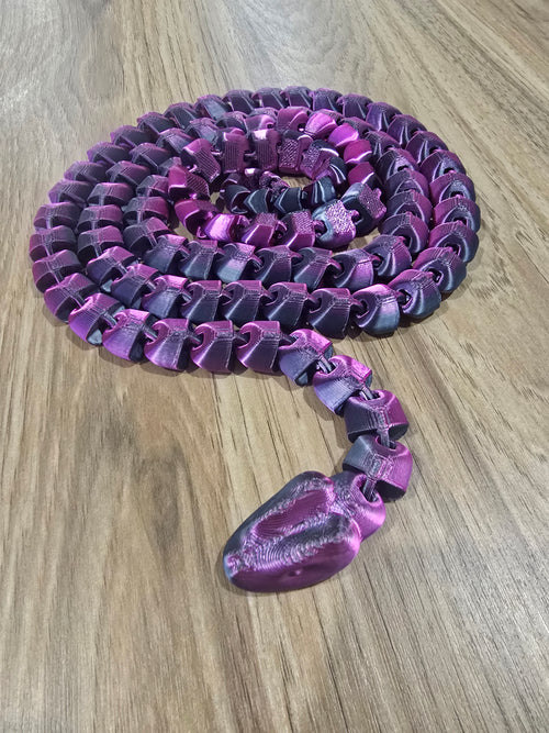 3D printed articulated dragon in purple, coiled on a wooden surface